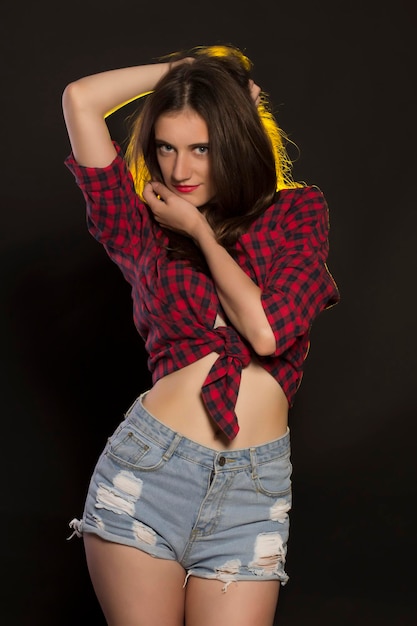 Seductive brunette woman in jeans shorts and a plaid shirt