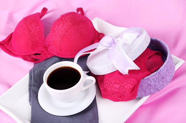 Seductive lingerie in present box and tray with cup of coffee on bed closeup