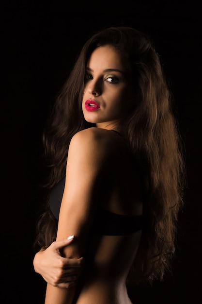 Seductive tanned young woman with bright makeup and long hair posing in black bra. Shadow and light