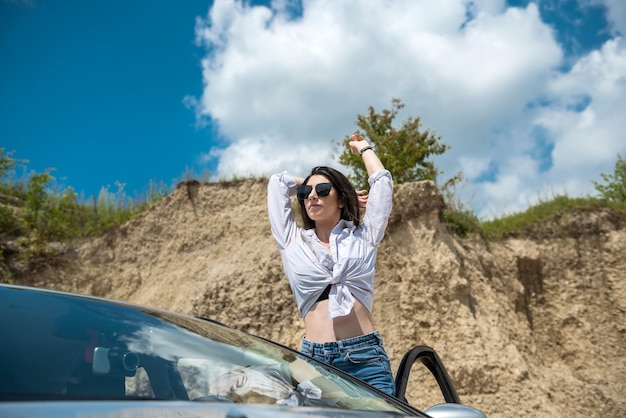 Seductive woman posing near car in summer outside the city enjoying freedom