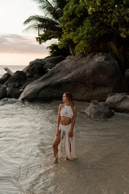 Donna seducente in abito bianco all'uncinetto boho in posa sulla spiaggia. foto di moda per vacanze estive e tropicali. intera lunghezza.