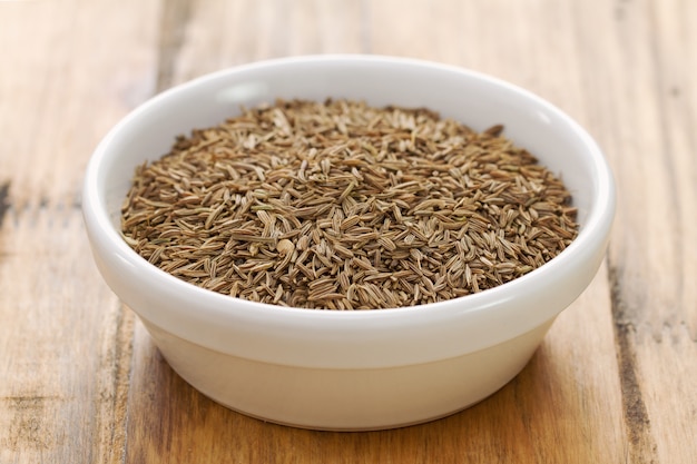 Seeds of carum in white bowl on brown wooden background