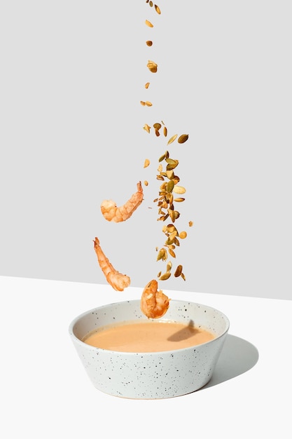 Photo seeds and shrimp fall into the pumpkin cream soup white background flying food