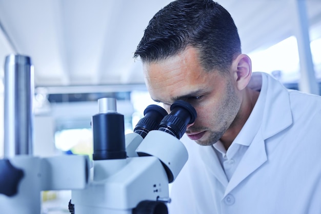 Видеть вещи, недоступные человеческому глазу Обрезанный снимок красивого молодого ученого-мужчины, работающего с микроскопом в своей лаборатории