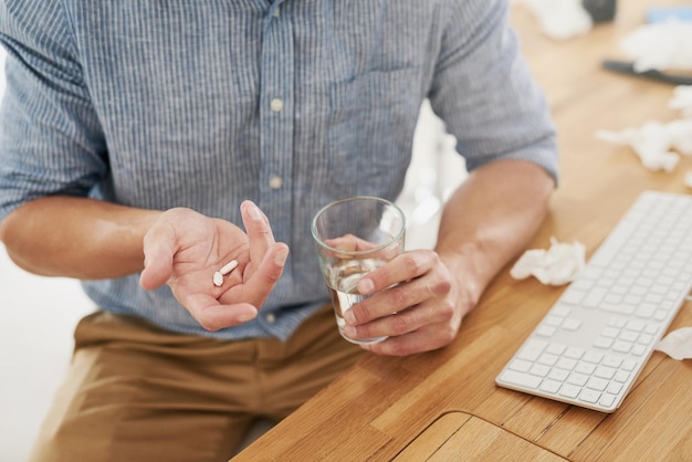 Seeking relief from pain Closeup shot of an unrecognisable businessman holding a glass of water and medication in an office