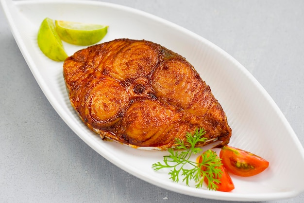 Seer fish fry arranged beautifully and garnished with onion lemon and tomato slices on white ceramic plate with grey textured background