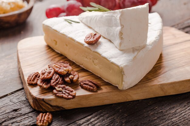 Segmento di brie o di mucca morbida - camembert francese su tavola di legno con uva, nido d'ape e noci pecan.