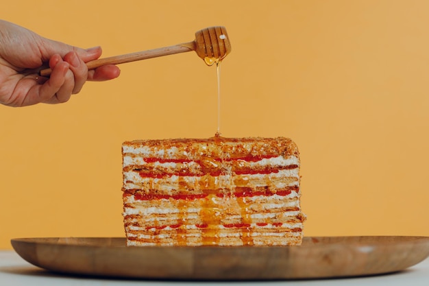 Segment van gelaagde honingcake met stok in de hand op plaat gele achtergrond