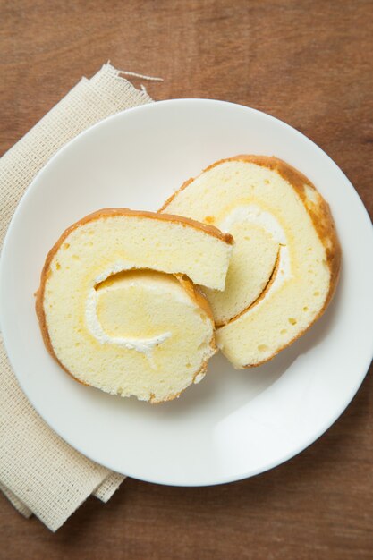 Segmenten van vanille roll cake in witte plaat op houten tafel.