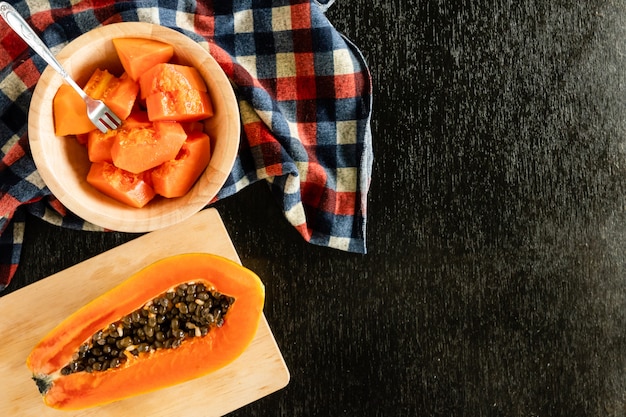 Segmenten van zoete papaya in houten kom op zwarte tafel. kopie ruimte