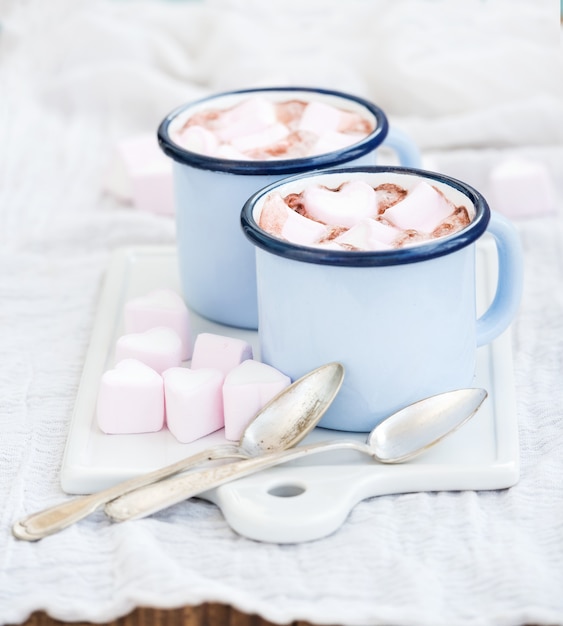 Seint Valentine's holiday greeting set. Hot chocolate and heart shaped marshmallows in old enamel mugs on white ceramic serving board 