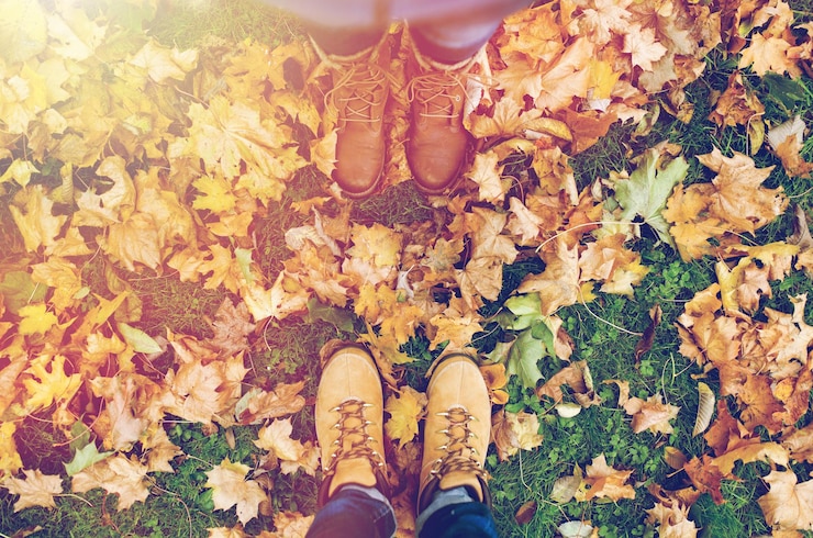 Foto seizoen en mensen concept - paar voeten in laarzen met herfst bladeren op de grond