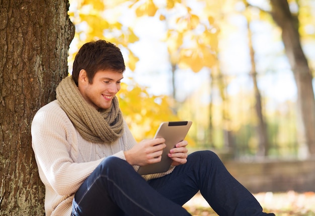 seizoen, technologie en mensen concept - lachende jonge man met tablet pc-computer in herfst park