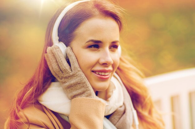 Foto seizoen, technologie en mensen concept - mooie gelukkige jonge vrouw met koptelefoon luisteren naar muziek en zitten op een bankje in het herfstpark