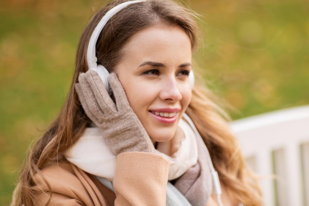 Foto seizoen, technologie en mensenconcept - mooie gelukkige jonge vrouw met koptelefoon die naar muziek luistert en op een bankje zit in het herfstpark