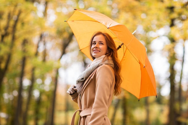 seizoen, weer en mensenconcept - mooie gelukkige jonge vrouw die met gele paraplu in de herfstpark loopt