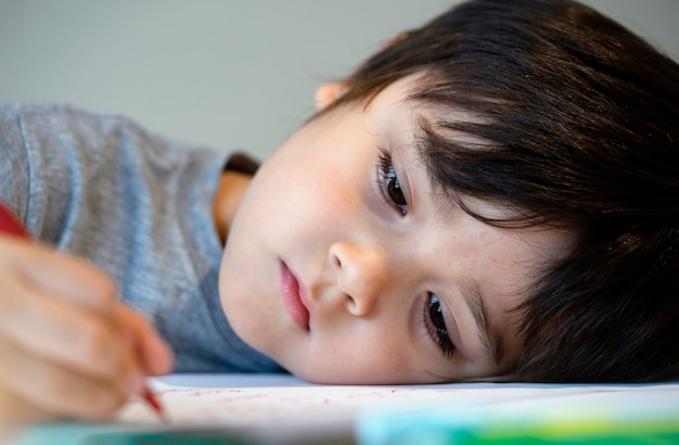 Selctive focus lonely child boy lying head down on table with sad face, Emotional portrait of Five years old kid bored with school homework, Spoiled child