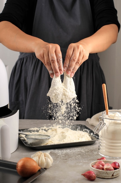 Selected focus on drumstick, female home chef making homemade\
crispy fried chicken, coating chicken drunsticks with flour in the\
kitchen, action photography