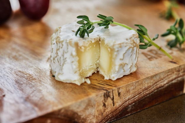 Foto formaggi francesi selezionati con uva, su tavola di legno con rosmarino e coltello.