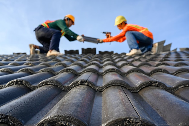 Selecteer de focus op dakpannen onscherpe achtergrond van een dakdekker die op het dak van een huis werkt gebruik een boor om de schroeven te boren om de cementtegels te bevestigen