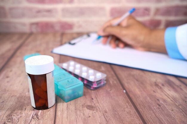 Selectieve aandacht. arts schrijven op papier en pillen contianer op kliniek tafel.