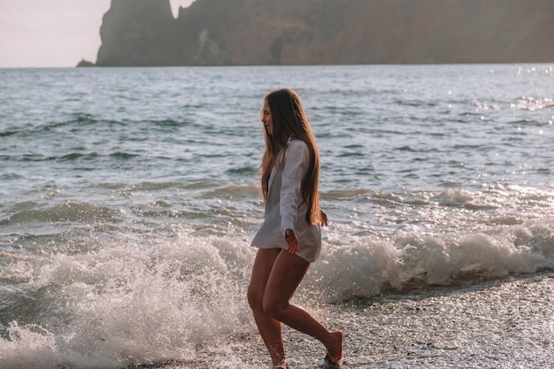 Selectieve aandacht gelukkige zorgeloze sensuele vrouw met lang haar in zwarte badmode poseren bij zonsondergang strand