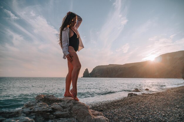 Selectieve aandacht gelukkige zorgeloze sensuele vrouw met lang haar in zwarte badmode poseren bij zonsondergang strand