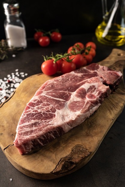 Selectieve aandacht. rauwe biefstuk van gemarmerd varkensvlees in rustieke stijl. voor het koken. op een houten bord, met grof zout en kruiden. rustig, close-up