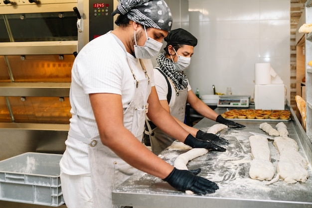 Selectieve aandacht van twee latino bakkers die deeg voor brood kneden met gezichtsmasker en handschoenen