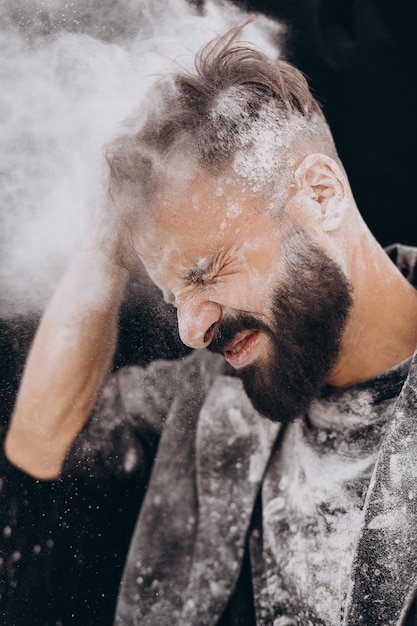 Selectieve focus geluidseffect stijlvol portret van een jonge, bebaarde man in zwarte kleding op een zwarte achtergrond De man is bezaaid met witte stof