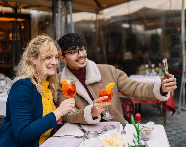 Selectieve focus op een lachend blond meisje dat een selfie maakt met haar vriend terwijl ze iets drinken