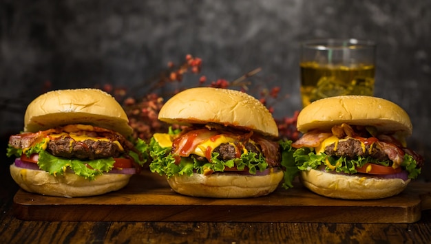 Selectieve focus op hamburgers met runderburgers, gebakken uien, spinazie, ketchup en kaas. Geserveerd met bier op houten plank loft achtergrond.