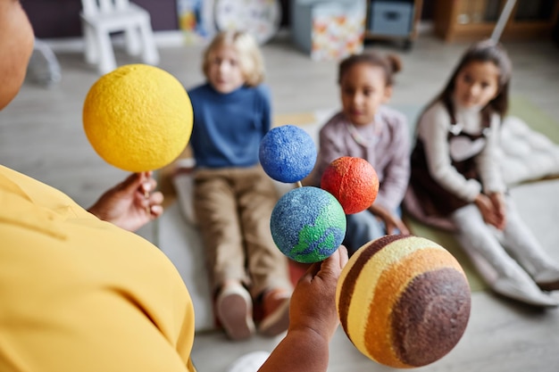 Selectieve focus op planeetmodellen van het zonnestelsel die worden vastgehouden door een leraar die voor een groep intercul staat