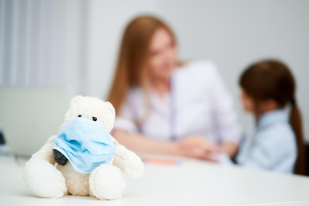 Foto selectieve focus teddybeer met medisch masker in ziekenhuis met vrouwelijke blanke arts en kind