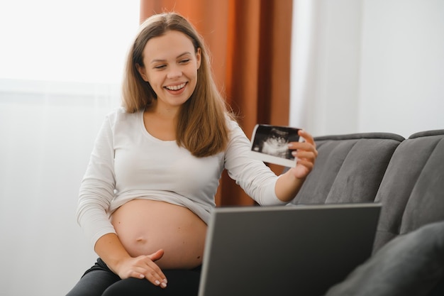 Selectieve focus van gelukkige zwangere vrouw die ultrasone foto's laat zien tijdens een videogesprek