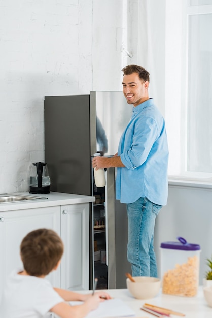 Selectieve focus van glimlachende vader met peuterzoon die tijdens het ontbijt in de keuken tekent