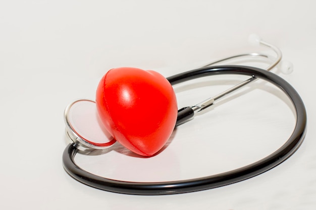 Selectieve focus van stethoscoop op wit oppervlak met een rood hart, medisch concept