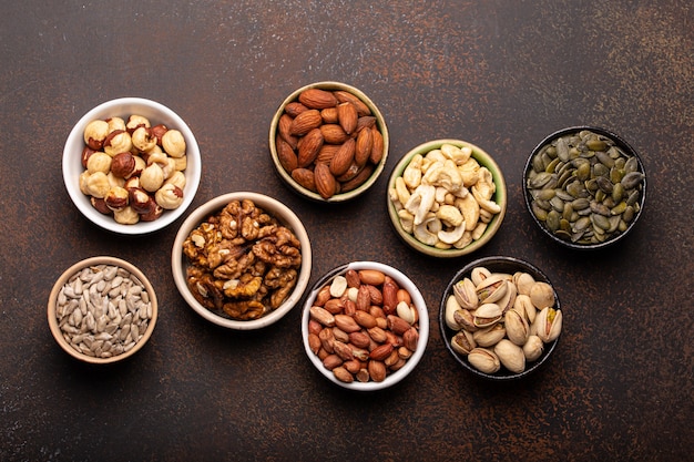 Selezione di noci crude assortite e semi vari in ciotole su sfondo di pietra marrone dall'alto, sana fonte di energia, grassi e proteine vegetariane