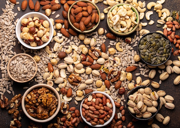 Selection of assorted raw nuts and various seeds in bowls on brown stone background from above, healthy source of energy, fat and vegetarian protein