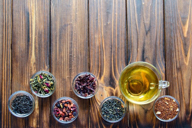 Selection of assorted teas in transparent little bowls on natural wooden background