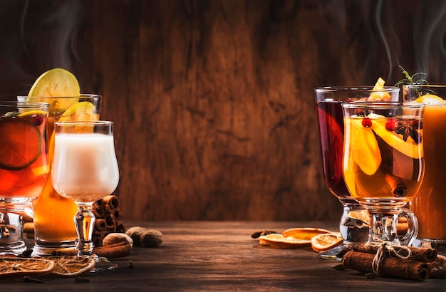 Selection of autumn or winter seasonal alcoholic hot cocktails mulled wine glogg grog eggnog warm ginger ale hot buttered rum punch mulled apple cider on wood background copy s