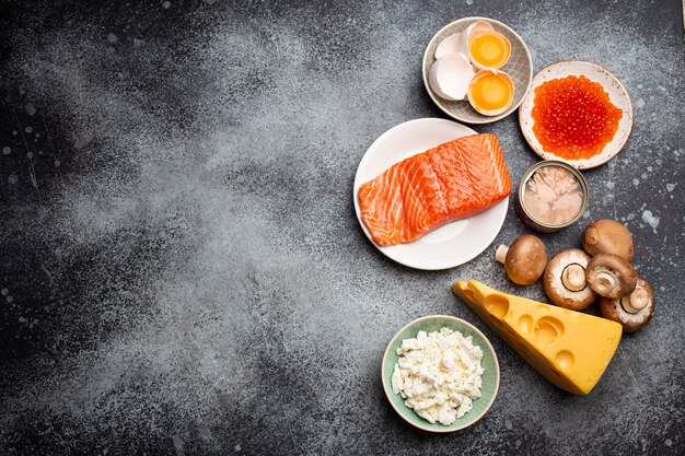 Selection of natural sources of vitamin D: fresh salmon, caviar, cheese, mushrooms, tuna, eggs on gray stone background top view. Foods and products rich in vitamin D. Template or space for text