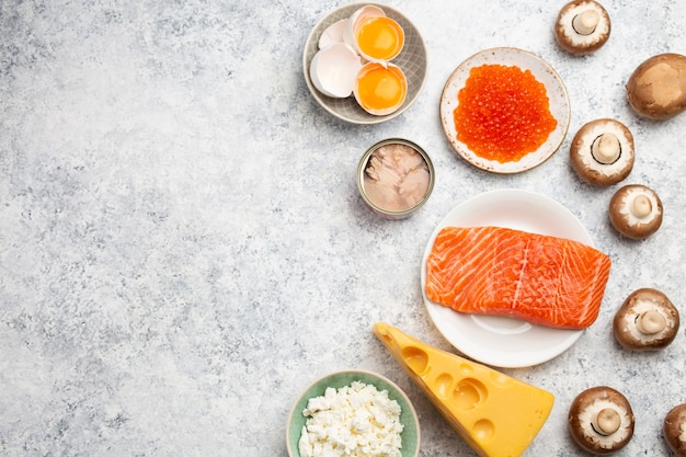 Selection of natural sources of vitamin D: fresh salmon; caviar; cheese; mushrooms; tuna; eggs on white stone background top view. Assorted foods and products rich in vitamin D; from above; copy space