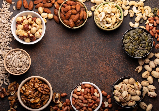 Фото Ассорти из сырых орехов и различных семян в мисках на коричневом каменном фоне сверху, здоровый источник энергии, жир и вегетарианский белок, место для текста