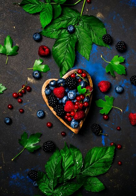 Selection of summer berries in heart shape bowl food background top view