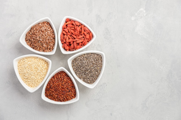 Selection of super foods in white bowls on gray concrete background.