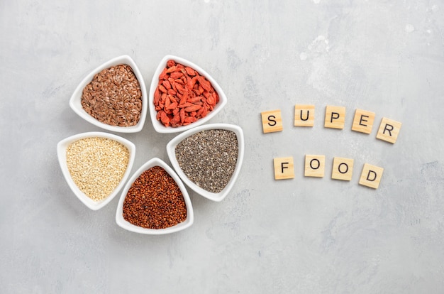 Selection of super foods in white bowls on gray concrete background.