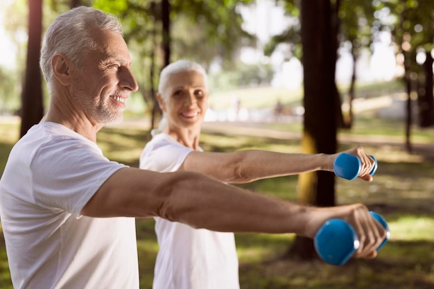 Selective focus of aged man keeping his arm with weight in front of him and exercising with his wife