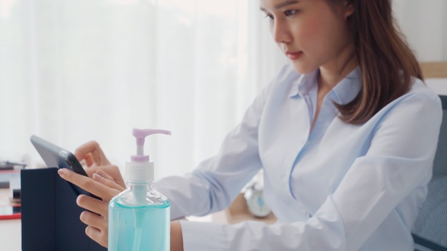 Foto il fuoco selettivo della bottiglia del gel dell'alcool sulla tavola, donna che lavora nel fondo della sfuocatura ha preparato il gel disinfettante per lavaggio della mano per pulire germe, batteri e virus. protezione pandemica e concetto di assistenza sanitaria.