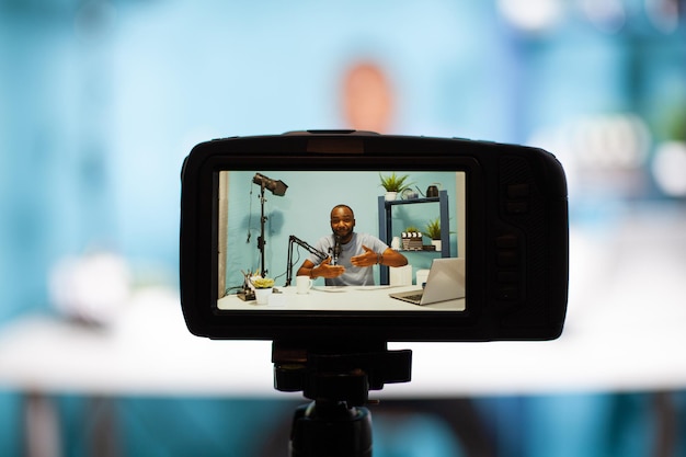 Selective focus on back screen of dslr filming social media influencer hosting live talk in vlogging studio. Closeup of professional digital camera recording content creator talking in live podcast.